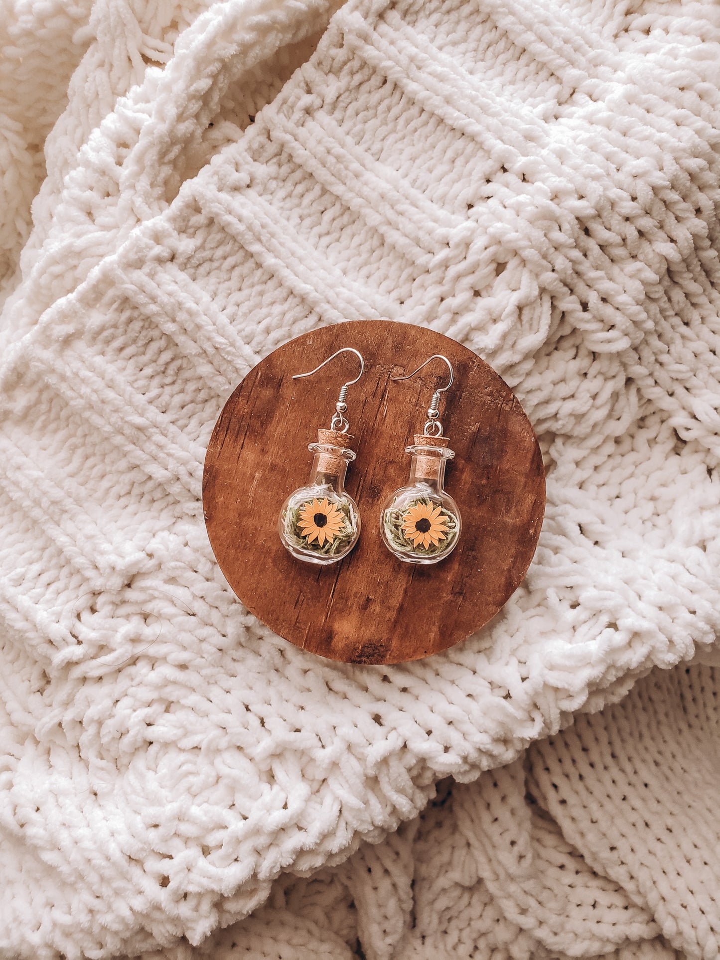 paper sunflowers in tiny glass jar earrings laying on a small wood coaster on top of a cozy blanket - Novel Blossoms Co