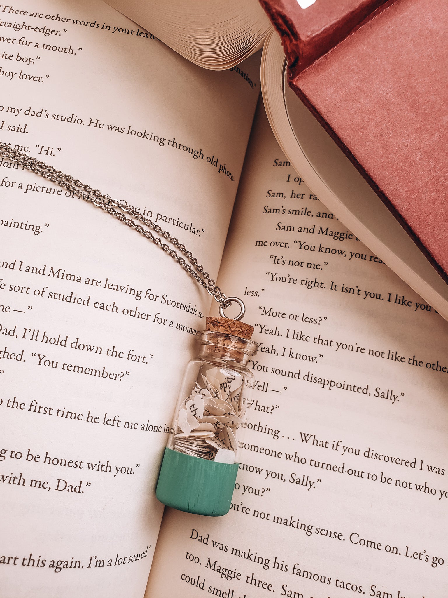 A wish jar bookish necklace lying on an open book - Novel Blossoms Co