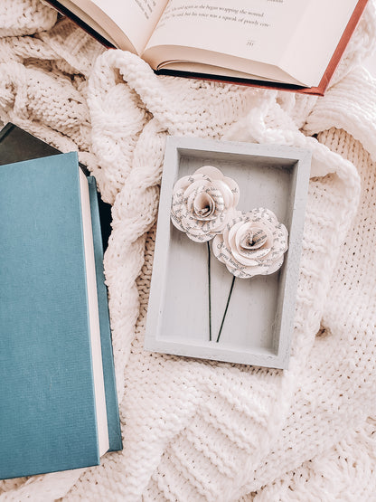 framed paper flowers made from book pages lying on a cable-knit sweater blanket and books scattered around - Novel Blossoms Co