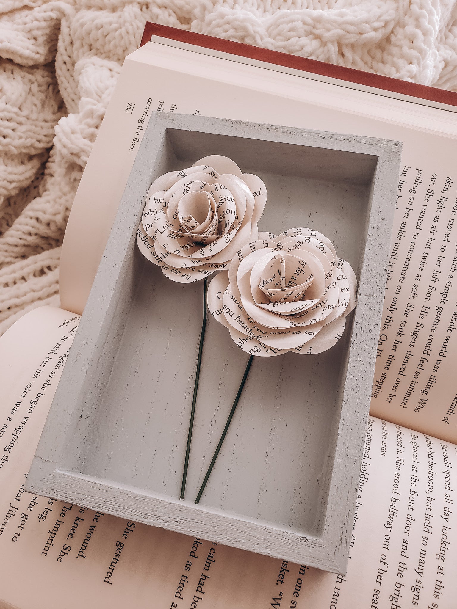 a pair of book page paper roses in a portrait shaped frame on an open book - Novel Blossoms Co