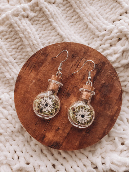 paper book page flowers in tiny glass jar earrings laying on a small wood coaster on top of a cozy blanket - Novel Blossoms Co