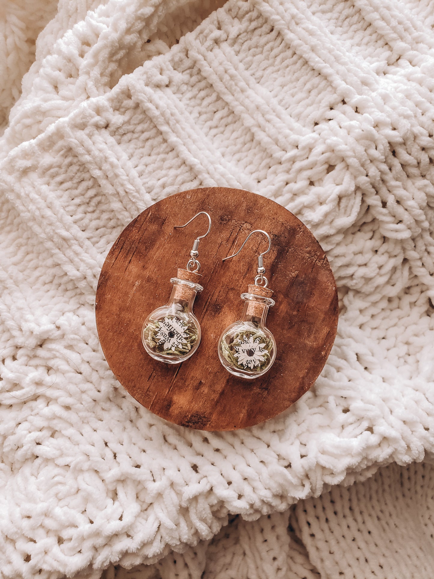 paper book page flowers in tiny glass jar earrings laying on a small wood coaster on top of a cozy blanket - Novel Blossoms Co